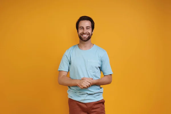 Handsome young man in casual clothing looking at camera and smiling while standing against yellow background — Stock Photo, Image