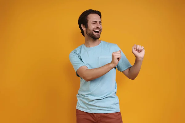 Счастливый молодой человек в повседневной одежде танцует на жёлтом фоне — стоковое фото