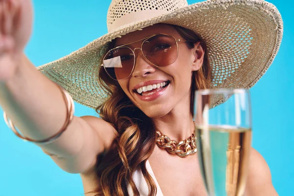 Hermosa joven sonriente mujer en sombrero elegante sosteniendo flauta de champán y haciendo selfie —  Fotos de Stock