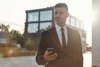 Ofis binasının yanında dururken elinde cep telefonu tutan kendinden emin bir iş adamı.