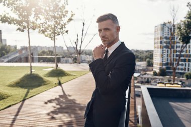 Düşünceli, olgun bir iş adamı dışarıda dikilirken çenesini tutuyor.