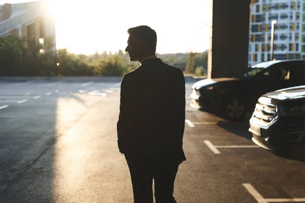 Silhoette de homem em formalwear de pé no estacionamento com pôr do sol no fundo — Fotografia de Stock
