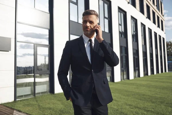 Zelfverzekerde volwassen zakenman praten op mobiele telefoon terwijl staan in de buurt van kantoorgebouw — Stockfoto