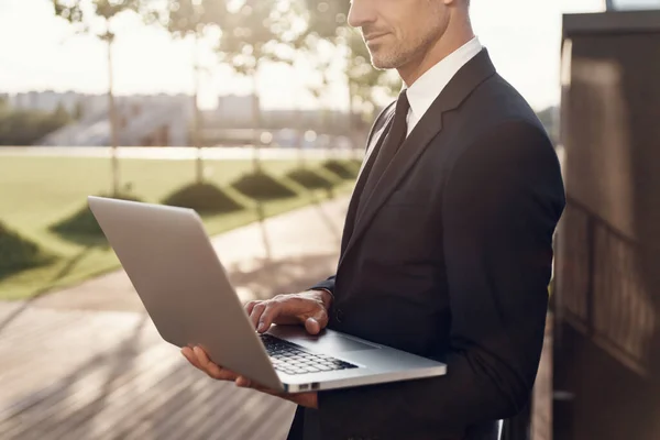 Gros plan d'un homme d'affaires mature confiant travaillant sur un ordinateur portable tout en restant debout à l'extérieur — Photo