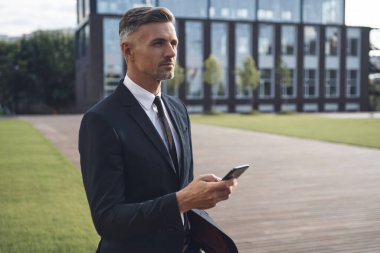 Ofis binasının yanında dururken cep telefonu tutan kendinden emin bir iş adamı.