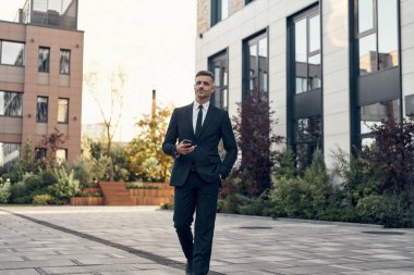 Ofis binasının yanında yürürken cep telefonu tutan kendinden emin bir iş adamı.