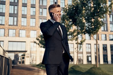 Ofis binasının yanında yürürken cep telefonuyla konuşan kendinden emin bir iş adamı.