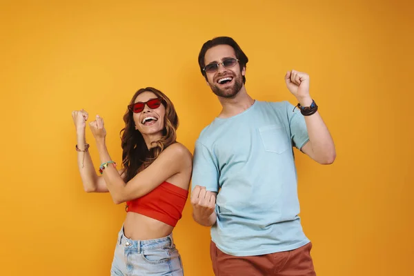 Beautiful young couple in eyeglasses having fun while standing against yellow background — Stock Photo, Image