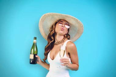 Zarif şapkalı, elinde şampanya şişesi olan ve bardak içen güzel, genç bir kadın.