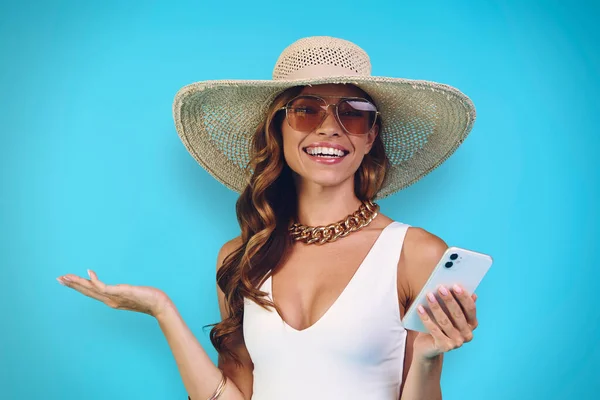 Happy young woman in elegant hat holding mobile phone and looking at camera — Stock Photo, Image