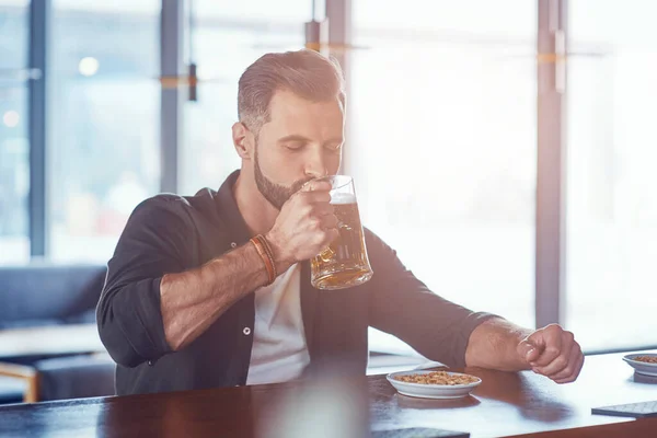 Jovem bonito em roupas casuais bebendo cerveja enquanto passava tempo no pub — Fotografia de Stock