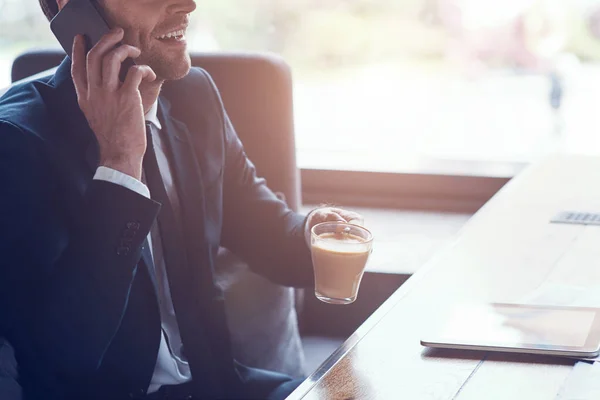 Usmívající se mladý podnikatel v plném obleku mluvit do chytrého telefonu, zatímco sedí v restauraci — Stock fotografie