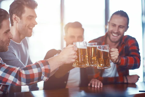Šťastní mladí muži v neformálním oblečení připíjeli jeden na druhého pivem a usmívali se — Stock fotografie