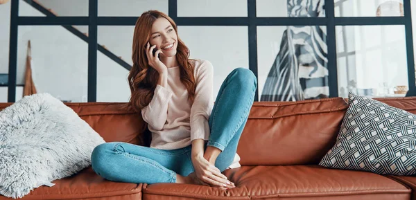 Glimlachende jonge vrouw het nemen van de telefoon, terwijl zitten op de bank thuis — Stockfoto