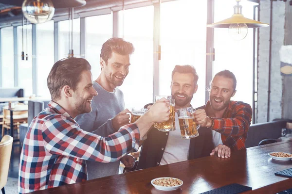 Jóvenes felices con ropa casual brindando entre sí con cerveza y riéndose mientras están sentados en el pub —  Fotos de Stock