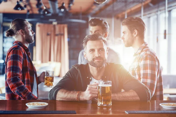 Schöner junger Mann in lässiger Kleidung trinkt Bier, während er Zeit mit Freunden in der Kneipe verbringt — Stockfoto