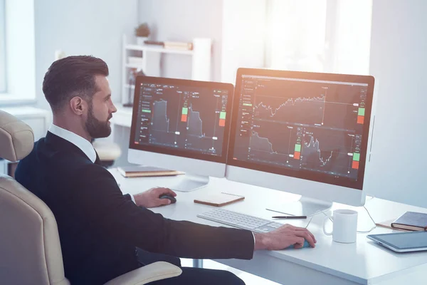 Seriös ung man i skjorta och slips analysera data på aktiemarknaden medan du arbetar på kontoret — Stockfoto