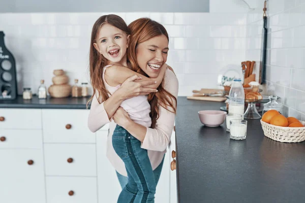 Mladá krásná milující matka objímající svou dceru a usmívající se při přípravě něco v kuchyni — Stock fotografie