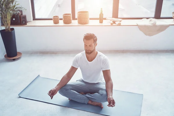 Vista dall'alto del bel giovane che fa yoga mentre è seduto in posizione di loto a casa — Foto Stock
