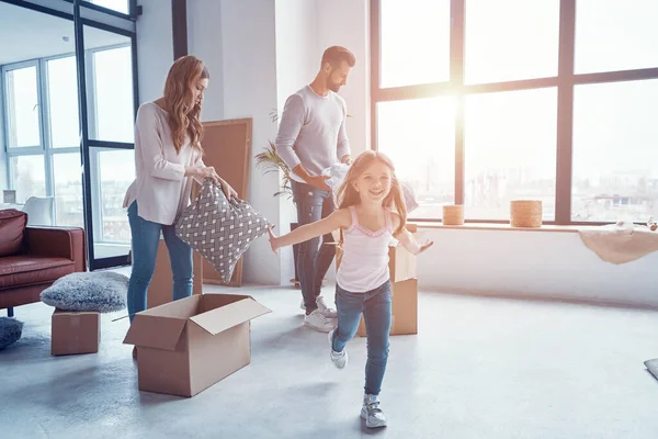 Χαρούμενη νεαρή οικογένεια χαμογελά και αποσυμπιέστε τα πράγματά τους, ενώ κινείται σε ένα νέο διαμέρισμα — Φωτογραφία Αρχείου