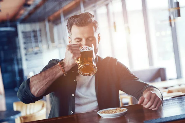 Charmanter junger Mann in lässiger Kleidung, der Bier trinkt, während er Zeit in der Kneipe verbringt — Stockfoto