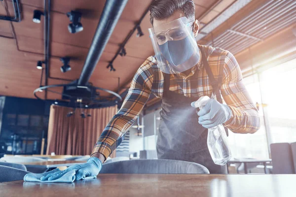 Jonge man in beschermende gezichtsscherm schoonmaak tafel in restaurant — Stockfoto