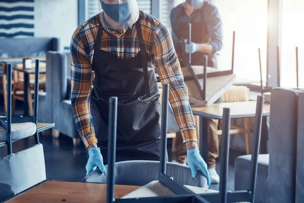 Three male waiters in protective workwear arranging furniture in restaurant — Stock Photo, Image