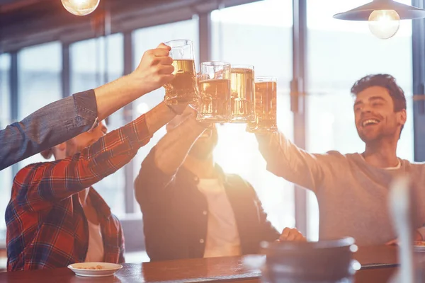 Glada unga män i vardagskläder skålar med öl och ler — Stockfoto