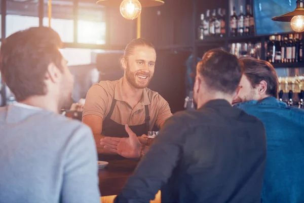 Cantinero alegre sirviendo cerveza a los jóvenes mientras está de pie en el mostrador del bar en el pub —  Fotos de Stock