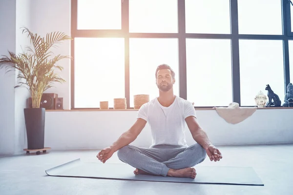 Bello giovane che fa yoga mentre è seduto in posizione di loto a casa — Foto Stock