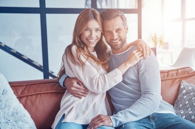 Güzel heteroseksüel çift evde vakit geçirirken kameraya bakıp gülümsüyor.