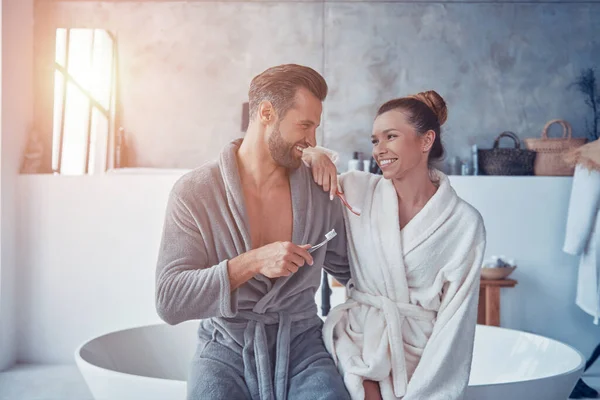Vackra unga par i badrockar ler och rengör tänderna medan du gör morgon rutin — Stockfoto