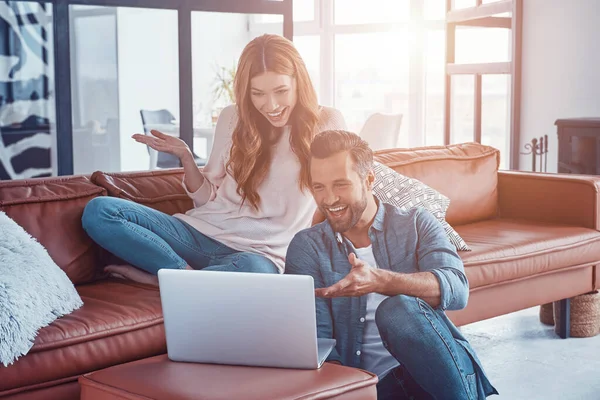 Bella giovane coppia che utilizza il computer portatile e sorridente mentre trascorre del tempo a casa — Foto Stock