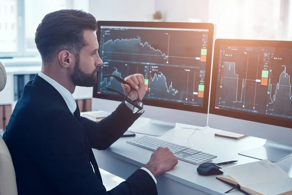 Koncentrerad ung man i skjorta och slips analysera data på aktiemarknaden medan du arbetar på kontoret — Stockfoto
