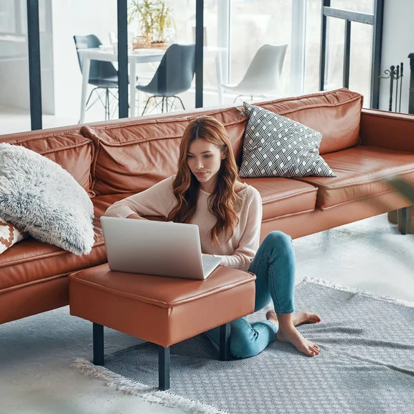 Beautiful young woman using laptop and smiling while spending time at home — Stock Photo, Image