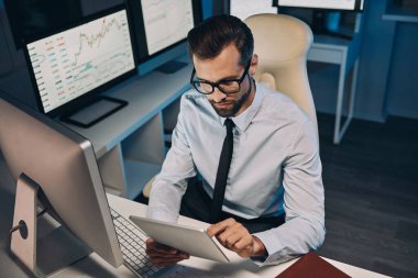 Ofiste geç saatlere kadar kalırken dijital tablet üzerinde çalışan kendine güvenen genç adamın en iyi görüntüsü.