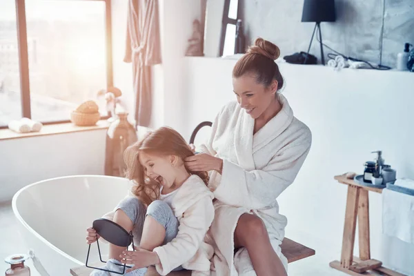 Beautiful young mother combining her daughters hair while doing morning routine — Stock Photo, Image