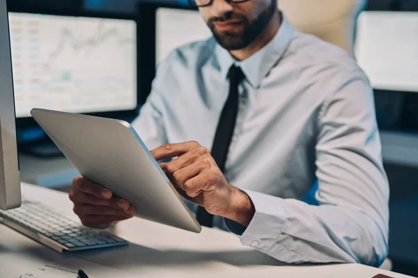 Close-up van geconcentreerde jongeman die aan digitale tablet werkt terwijl hij tot laat op kantoor blijft — Stockfoto