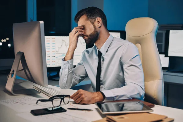 Jovem frustrado de camisa e gravata massageando o nariz e mantendo os olhos fechados enquanto fica até tarde no escritório — Fotografia de Stock