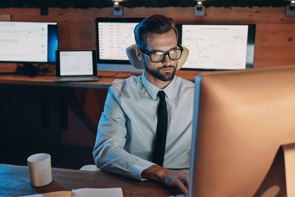 Selbstbewusster junger Mann arbeitet am Computer und bleibt spät im Büro — Stockfoto