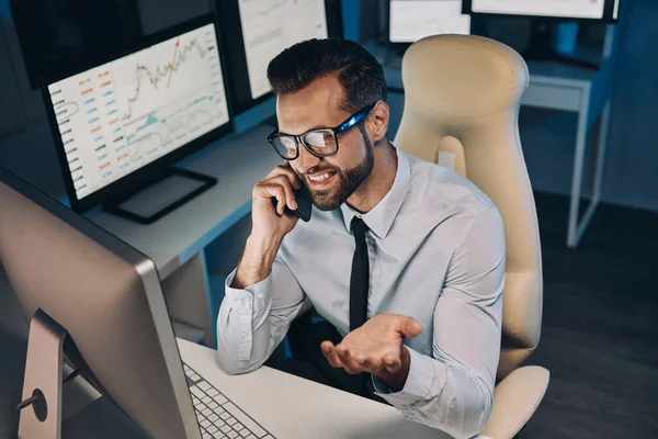 Vista superior de hombre joven feliz en camisa y corbata hablando en el teléfono móvil y mirando el ordenador — Foto de Stock