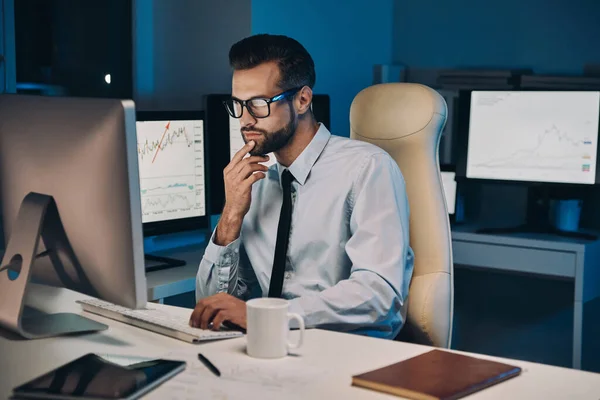 Konzentrierter junger Mann arbeitet am Computer, während er spät im Büro bleibt — Stockfoto