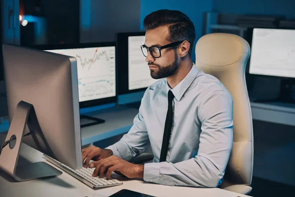 Selbstbewusster junger Mann arbeitet am Computer und bleibt spät im Büro — Stockfoto