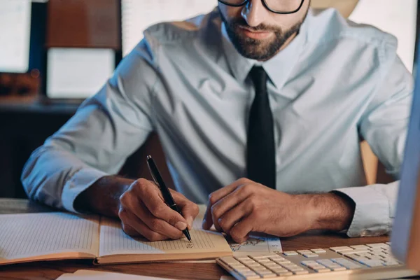 Close-up van zelfverzekerde jongeman maakt aantekeningen tijdens een verblijf in het kantoor — Stockfoto