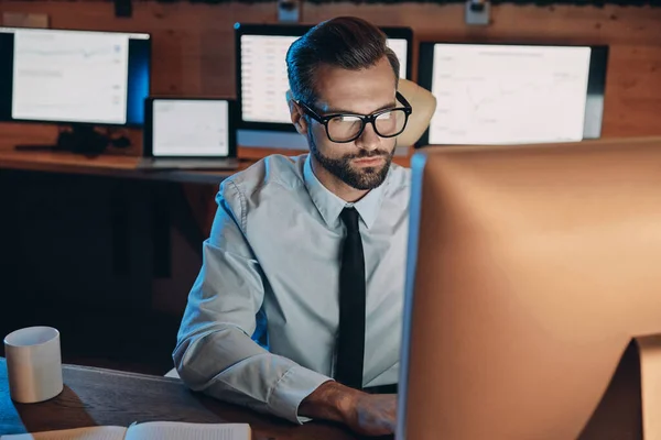 Jovem concentrado trabalhando no computador enquanto fica até tarde no escritório — Fotografia de Stock