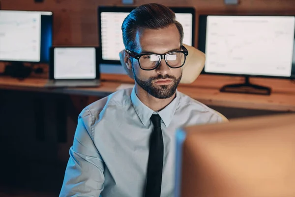 Уверенный молодой человек, работающий за компьютером, оставаясь допоздна в офисе — стоковое фото