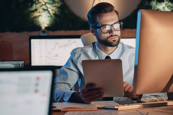 Jeune homme confiant travaillant sur ordinateur tout en restant tard au bureau — Photo