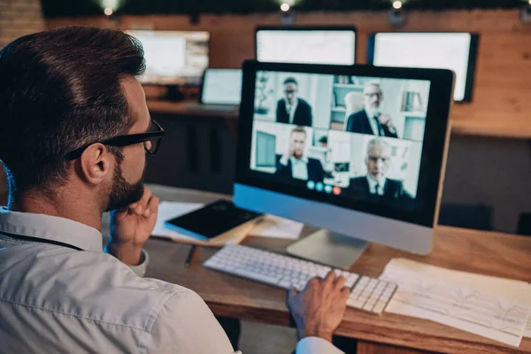 Jeune homme confiant ayant une vidéoconférence avec les collègues tout en restant tard dans le bureau — Photo