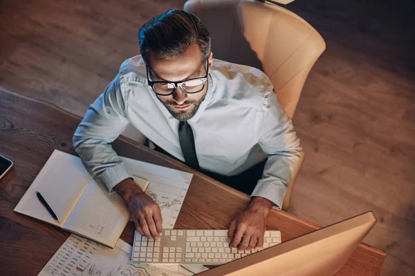 Vue de dessus du jeune homme concentré travaillant sur ordinateur tout en restant tard dans le bureau — Photo