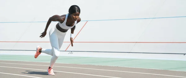 Mulher africana jovem confiante em roupas esportivas correndo na pista ao ar livre — Fotografia de Stock